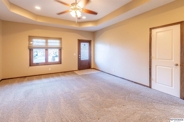 spare room featuring a tray ceiling, light carpet, and ceiling fan