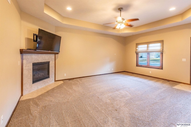 unfurnished living room with a tray ceiling, a premium fireplace, ceiling fan, and light colored carpet