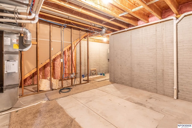 basement featuring heating unit and brick wall