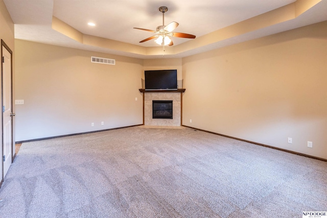 unfurnished living room with carpet, ceiling fan, a raised ceiling, and a fireplace