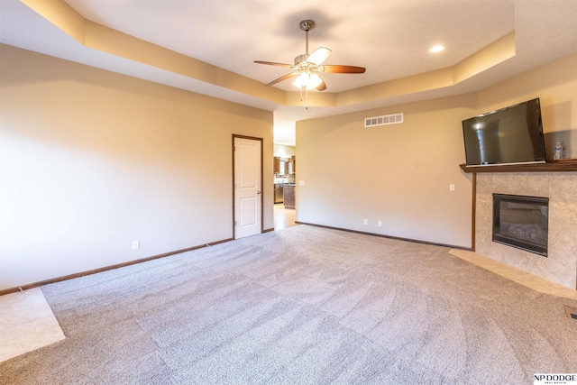 unfurnished living room featuring a tile fireplace, carpet, a tray ceiling, and ceiling fan