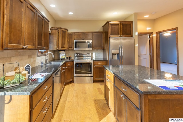 kitchen featuring appliances with stainless steel finishes, backsplash, dark stone counters, sink, and light hardwood / wood-style floors