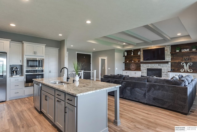 kitchen with sink, light stone counters, an island with sink, light hardwood / wood-style floors, and appliances with stainless steel finishes