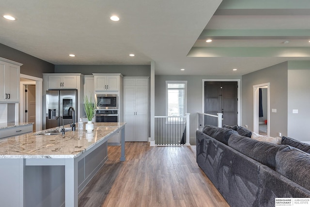 kitchen featuring a spacious island, hardwood / wood-style flooring, light stone countertops, white cabinetry, and stainless steel appliances