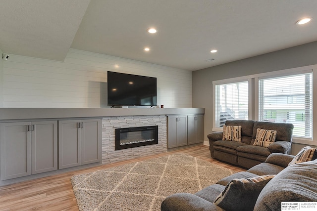 living room featuring a stone fireplace, a healthy amount of sunlight, and light wood-type flooring