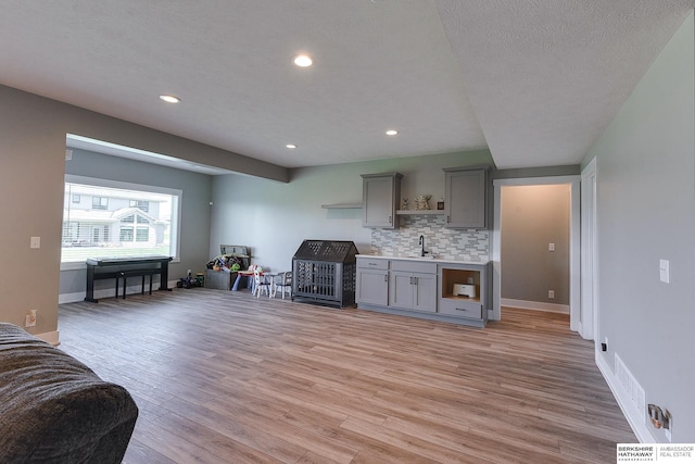 interior space featuring decorative backsplash, a textured ceiling, gray cabinets, and light hardwood / wood-style floors