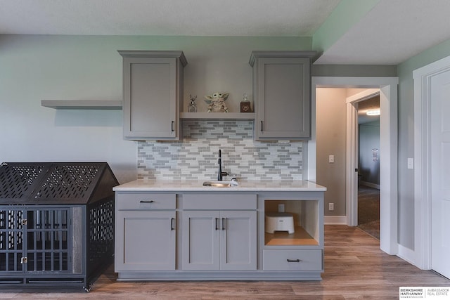 kitchen with backsplash, gray cabinets, light wood-type flooring, and sink