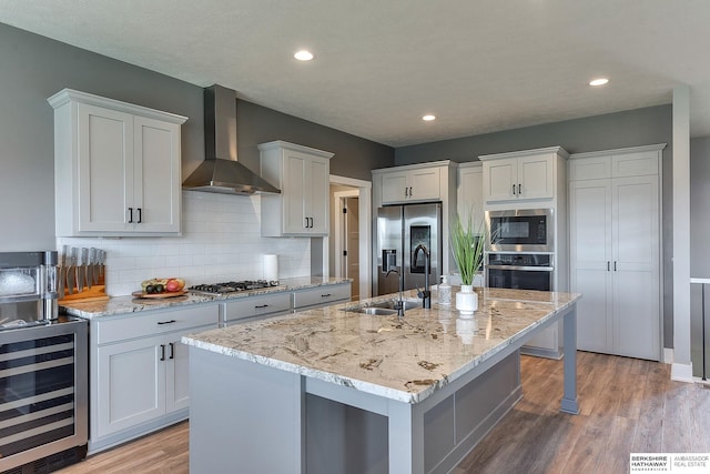 kitchen featuring white cabinetry, wall chimney exhaust hood, stainless steel appliances, wine cooler, and a kitchen island with sink