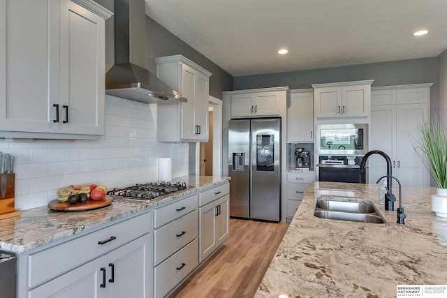 kitchen featuring stainless steel appliances, sink, wall chimney range hood, light hardwood / wood-style flooring, and white cabinetry