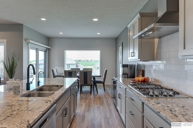 kitchen featuring light stone countertops, appliances with stainless steel finishes, sink, wall chimney range hood, and hardwood / wood-style flooring