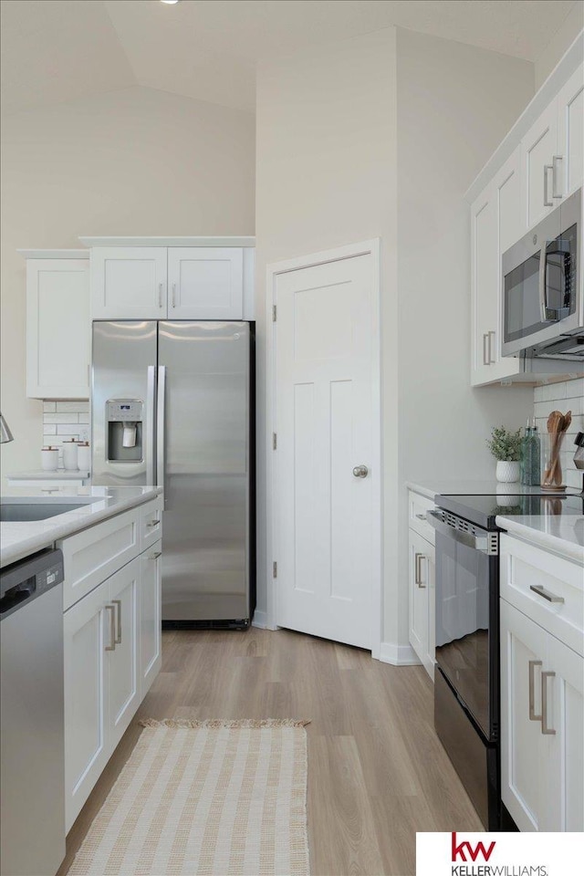 kitchen featuring backsplash, white cabinets, lofted ceiling, and appliances with stainless steel finishes