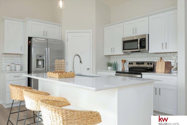 kitchen featuring backsplash, a kitchen bar, a kitchen island with sink, white cabinets, and appliances with stainless steel finishes