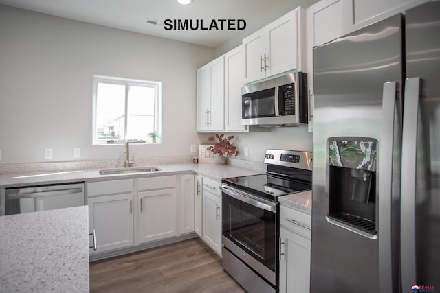 kitchen featuring light stone countertops, white cabinetry, sink, light hardwood / wood-style floors, and appliances with stainless steel finishes