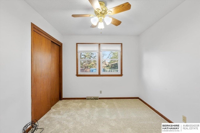 unfurnished bedroom with ceiling fan, a closet, light carpet, and a textured ceiling