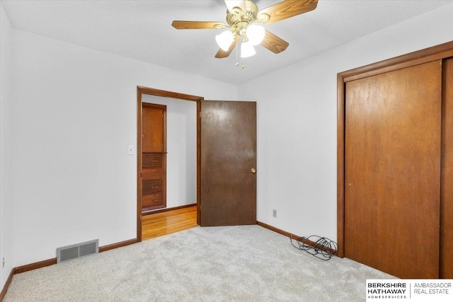 unfurnished bedroom featuring light carpet, ceiling fan, and a textured ceiling