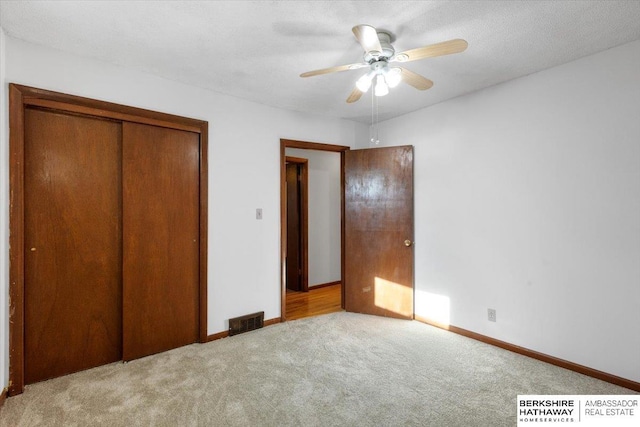 unfurnished bedroom featuring ceiling fan, a closet, light carpet, and a textured ceiling