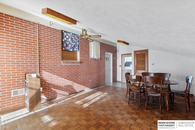 unfurnished dining area with ceiling fan, brick wall, a textured ceiling, and parquet flooring