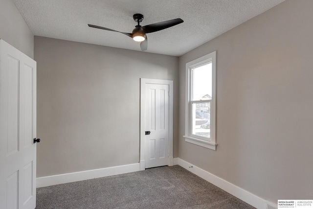 empty room featuring a healthy amount of sunlight, a textured ceiling, and dark carpet