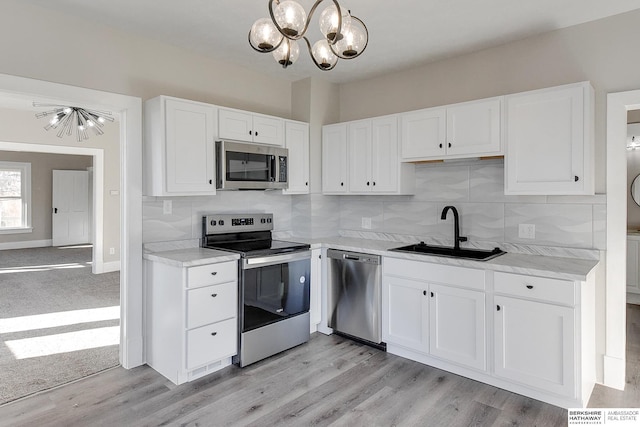 kitchen with sink, light wood-type flooring, appliances with stainless steel finishes, tasteful backsplash, and white cabinetry