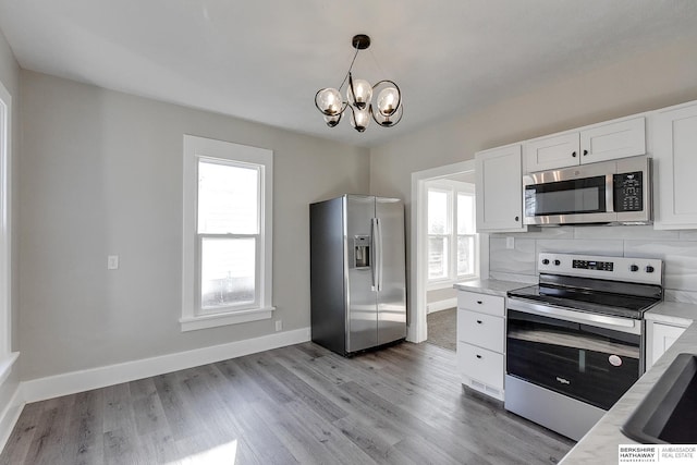 kitchen with pendant lighting, light hardwood / wood-style flooring, tasteful backsplash, white cabinetry, and stainless steel appliances