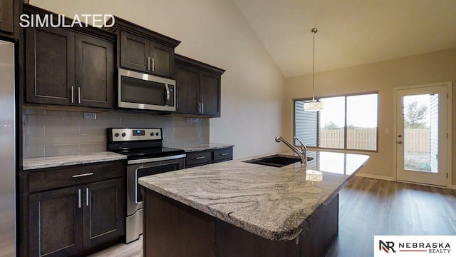 kitchen with appliances with stainless steel finishes, vaulted ceiling, a kitchen island with sink, and sink