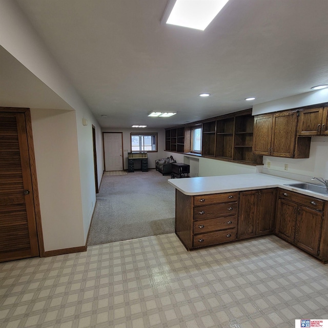 kitchen with kitchen peninsula, dark brown cabinets, light colored carpet, and sink