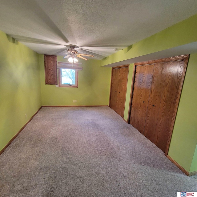 unfurnished bedroom featuring light carpet, a textured ceiling, two closets, and ceiling fan