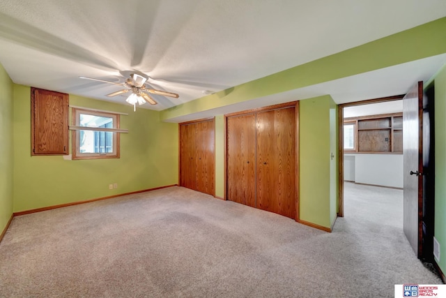 unfurnished bedroom with light carpet, ceiling fan, and multiple closets