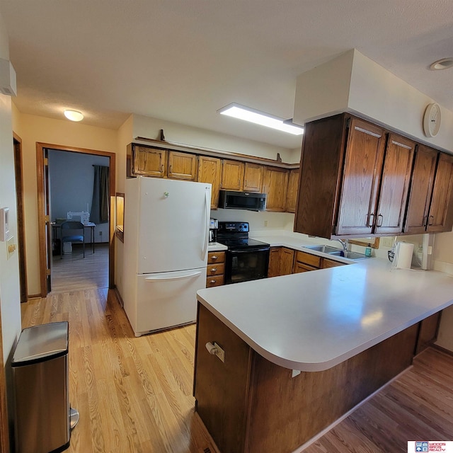 kitchen featuring black appliances, sink, light hardwood / wood-style flooring, a kitchen bar, and kitchen peninsula