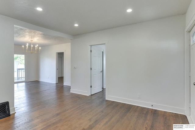 empty room featuring a chandelier, a textured ceiling, and dark wood-type flooring