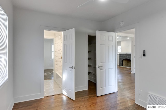 unfurnished bedroom featuring multiple windows, ceiling fan, hardwood / wood-style floors, and a fireplace