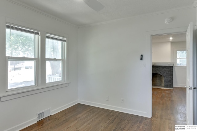 spare room featuring dark hardwood / wood-style floors, a healthy amount of sunlight, crown molding, and a brick fireplace