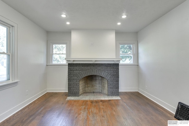 unfurnished living room with a wealth of natural light, dark hardwood / wood-style floors, and a brick fireplace