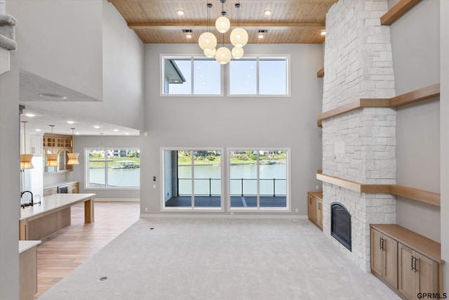 living room featuring a stone fireplace, a water view, wooden ceiling, and a towering ceiling