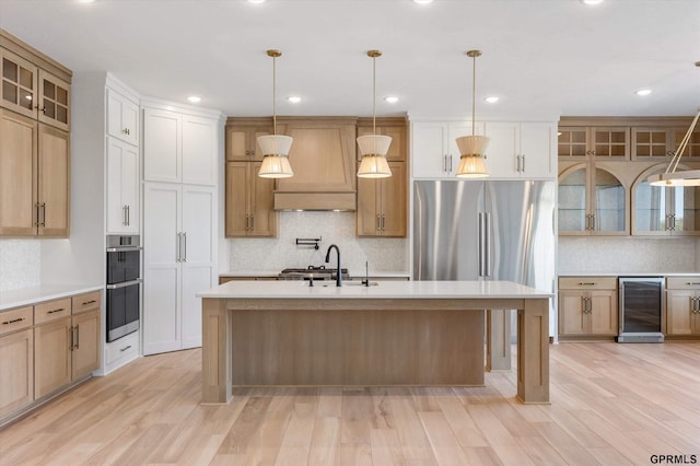 kitchen with light wood-type flooring, wine cooler, hanging light fixtures, and an island with sink