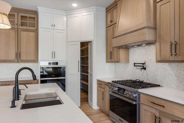 kitchen featuring custom exhaust hood, stainless steel appliances, sink, white cabinets, and light hardwood / wood-style floors