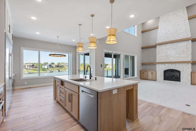 kitchen with pendant lighting, dishwasher, a kitchen island with sink, a stone fireplace, and sink