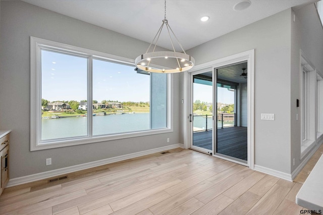 unfurnished dining area featuring plenty of natural light, a water view, light hardwood / wood-style floors, and an inviting chandelier