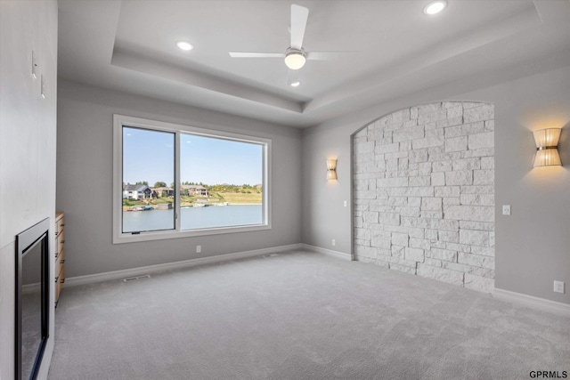 unfurnished living room featuring light carpet, a water view, a raised ceiling, and ceiling fan