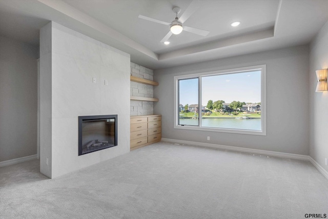 unfurnished living room featuring ceiling fan, a raised ceiling, light carpet, and a water view