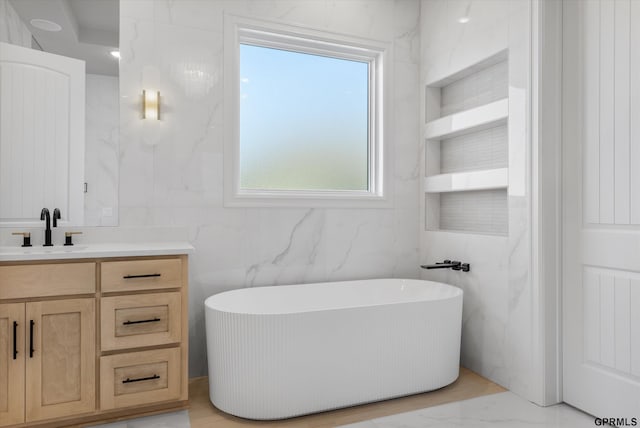 bathroom featuring vanity, a tub to relax in, a wealth of natural light, and tile walls