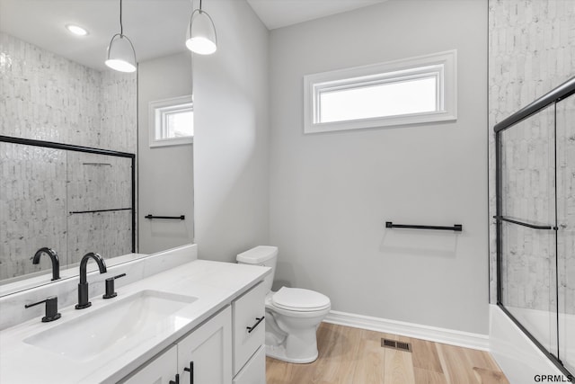 full bathroom featuring toilet, a healthy amount of sunlight, wood-type flooring, and shower / bath combination with glass door