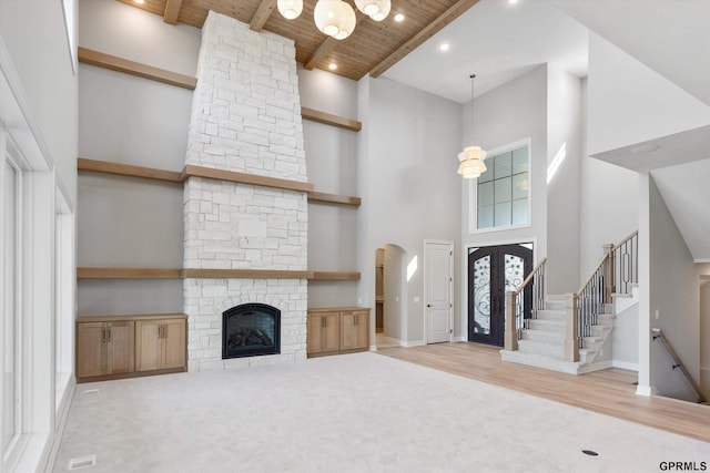 unfurnished living room featuring a towering ceiling, light hardwood / wood-style floors, a stone fireplace, and wooden ceiling