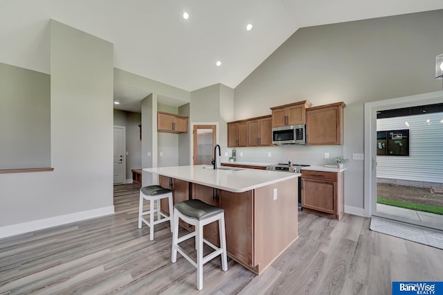 kitchen featuring light wood-type flooring, stainless steel appliances, a kitchen island with sink, sink, and high vaulted ceiling