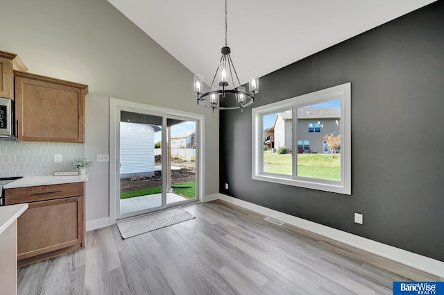 unfurnished dining area featuring high vaulted ceiling, light hardwood / wood-style flooring, and a notable chandelier