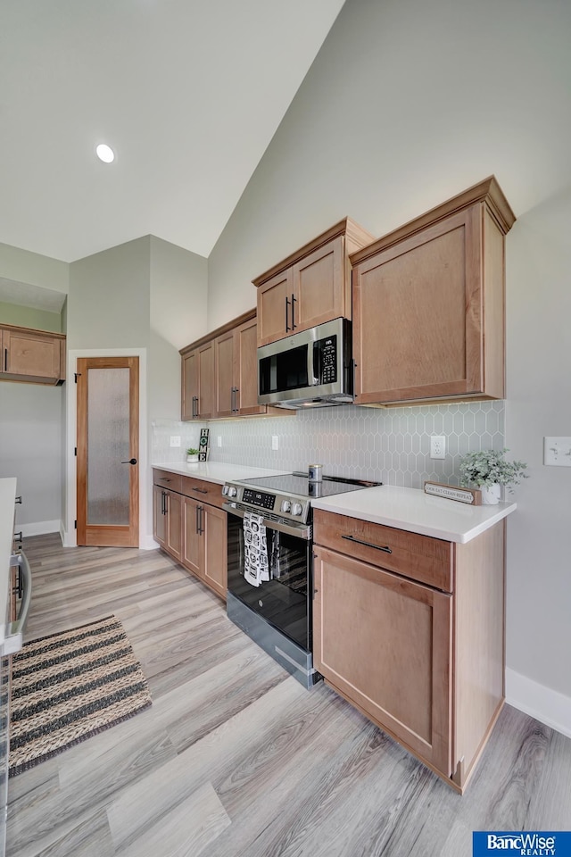 kitchen with high vaulted ceiling, light hardwood / wood-style floors, appliances with stainless steel finishes, and tasteful backsplash