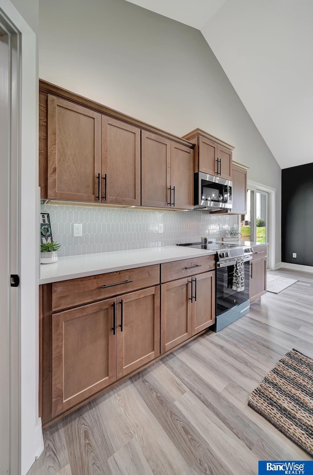 kitchen with stainless steel appliances, high vaulted ceiling, and light hardwood / wood-style flooring