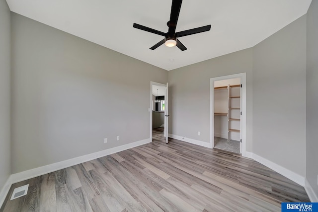 unfurnished bedroom with a closet, ceiling fan, light hardwood / wood-style flooring, and a spacious closet