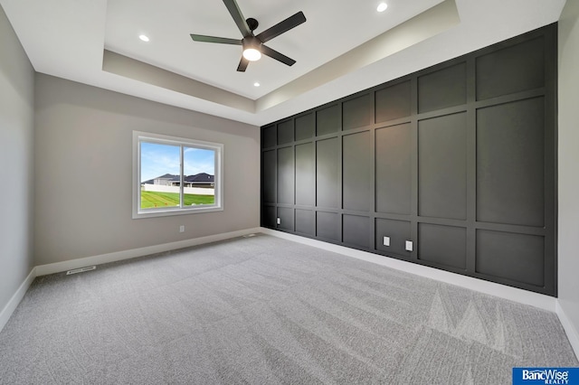 carpeted empty room with a raised ceiling and ceiling fan