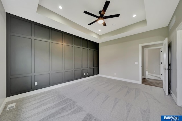 unfurnished bedroom featuring light carpet, a raised ceiling, and ceiling fan